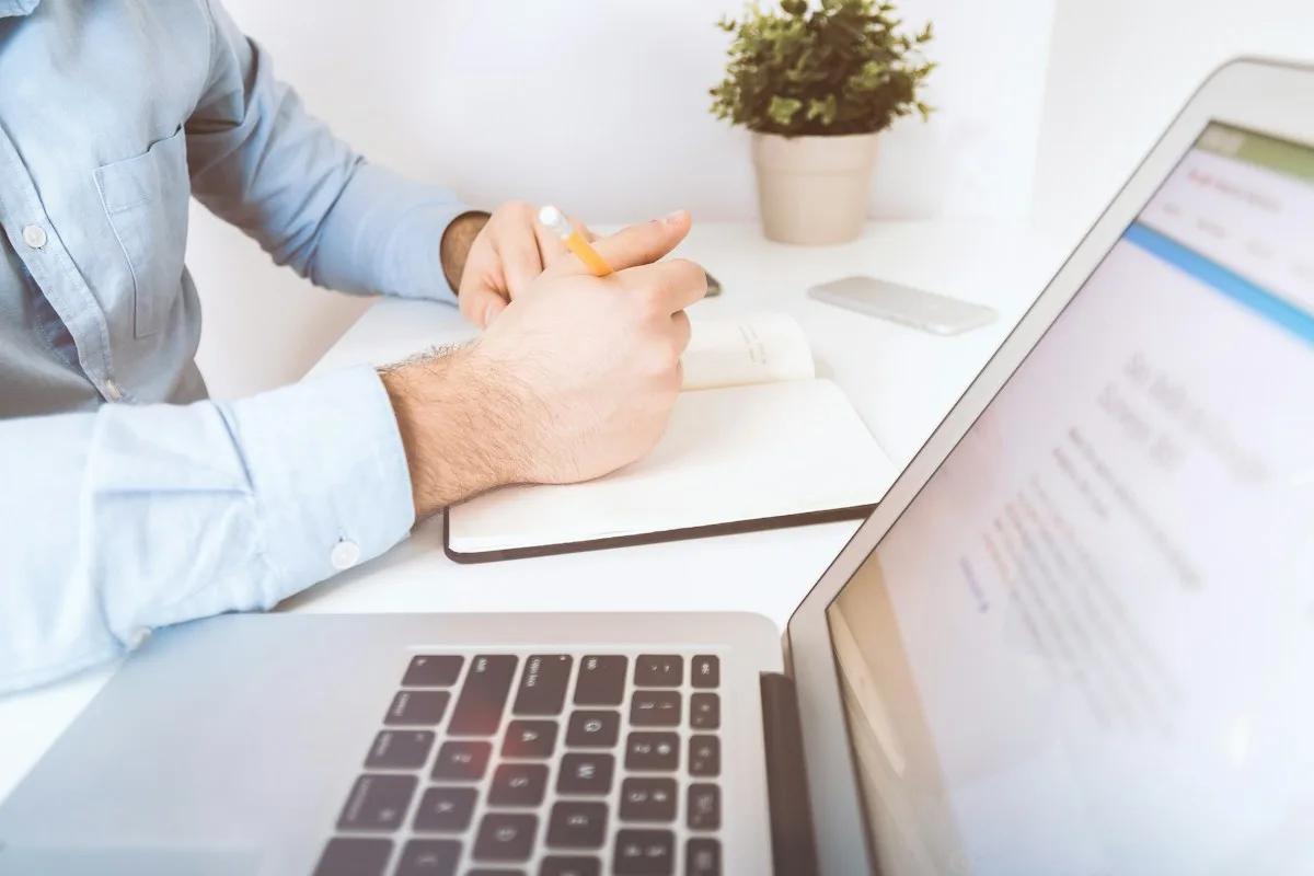 A writer making handwritten notes beside a laptop